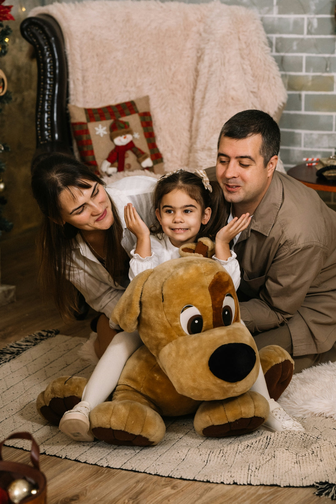 A man, woman and child sitting on the floor with a large stuffed dog