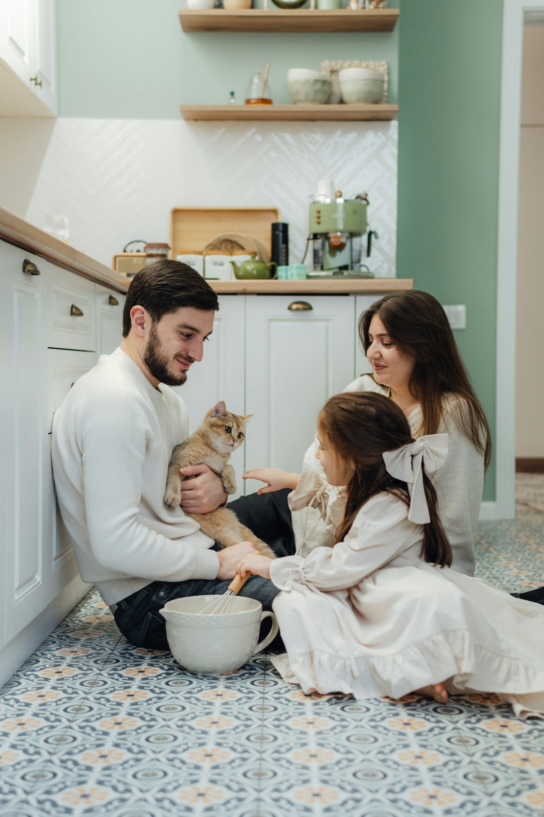 A man and two girls are sitting on the floor with a cat