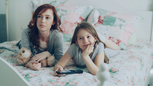 Mother and daughter watch television together on the bed