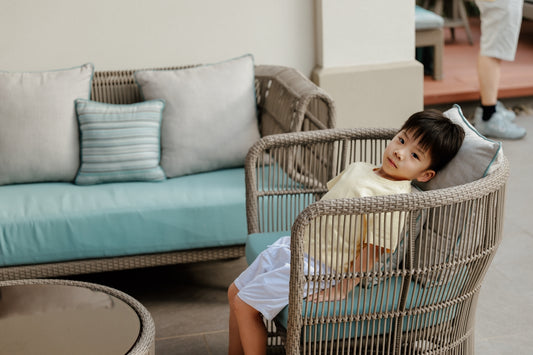A young boy relaxes on a wicker chair outdoors.