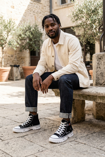 Black male model wearing black canvas high-top trainers with white platform soles